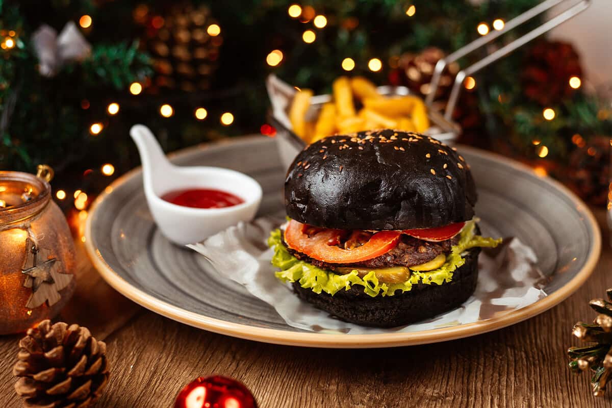 Saftiger Burger mit schwarzem Bun auf einem Teller und weihnachtliche Dekoration