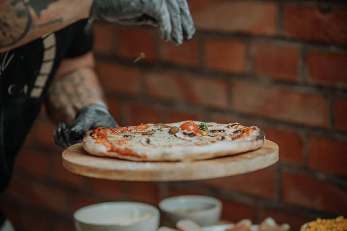 Mann verteilt frische Kräuter auf einer Pizza