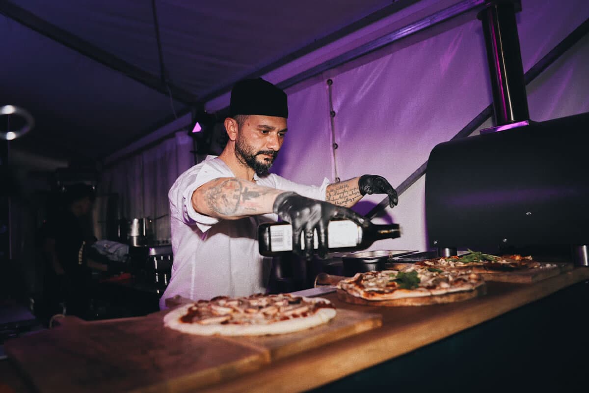 Mann träufelt Olivenöl über eine frische Pizza