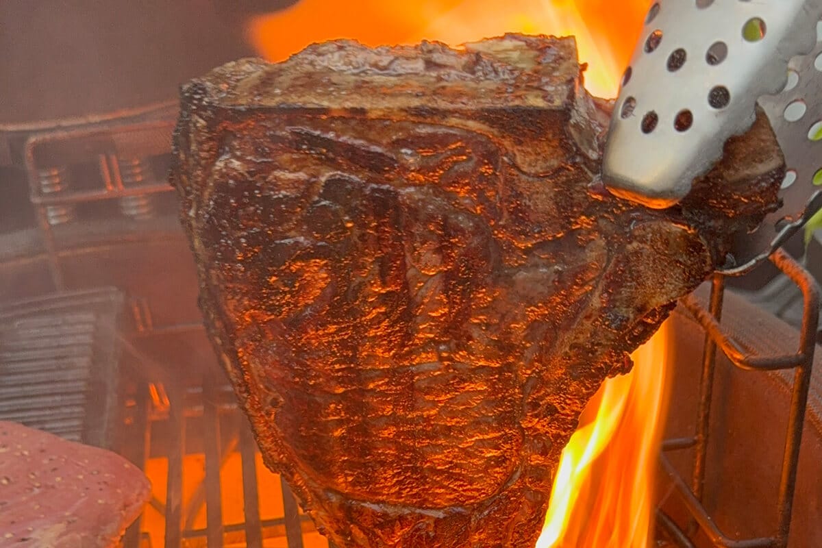 Saftiges Steak wird mit einer Zange in die Flamme eines Grills gehalten